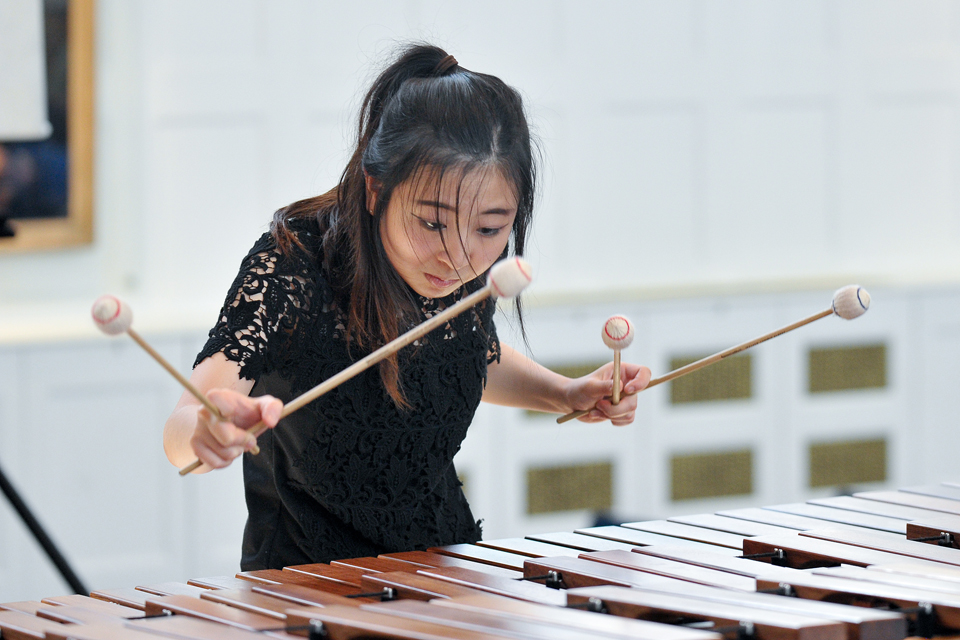 An Asian female student playing the marimba, in a well lit room.
